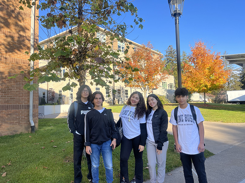 A sunny blue sky in the background and five high school students standing together smiling.
