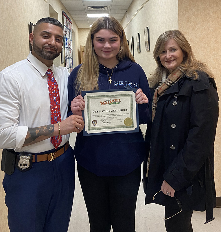 A man on the left and a woman on the right of a middle school student who is holding a certificate.