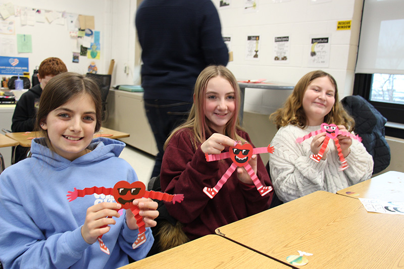 Three middle school girls smile, holding valentines they created.