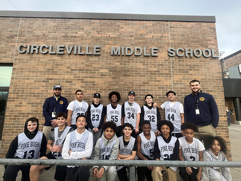 A team photo with a brick building in back that says Circleville Middle School. There are two rows of middle school boys, with men on either end in the back row. 