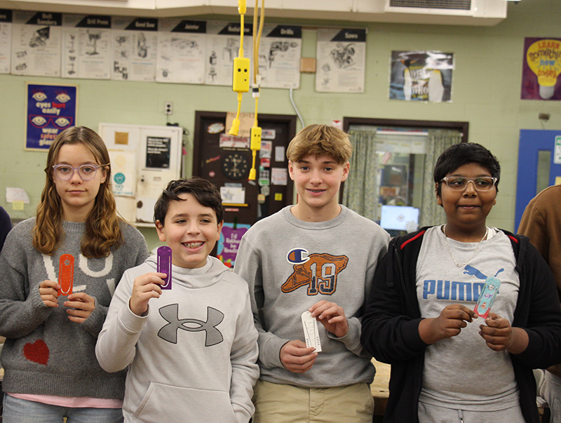 A group of four middle school students smile and hold their bookmarks they made.