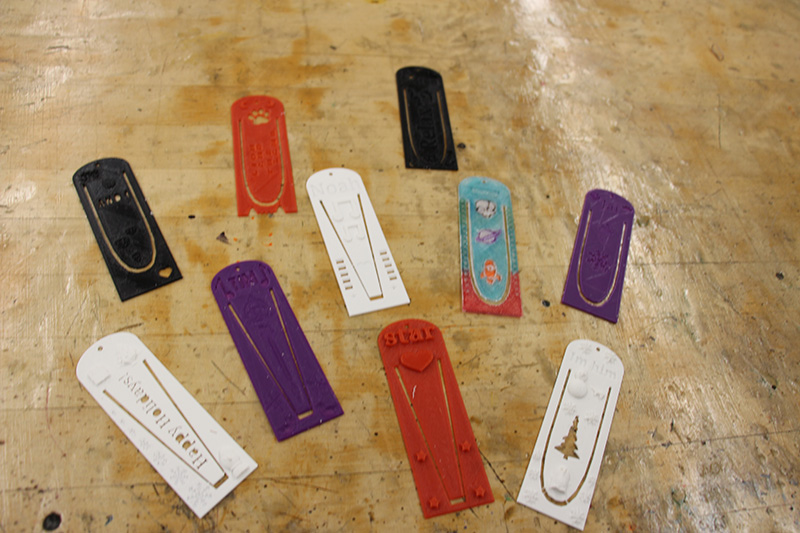 Ten bookmarks sit on a table. They are all different, different colors and designs, made by students and 3D printed.