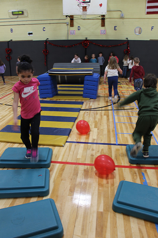 Younger elementary students run an indoor obstacle course..