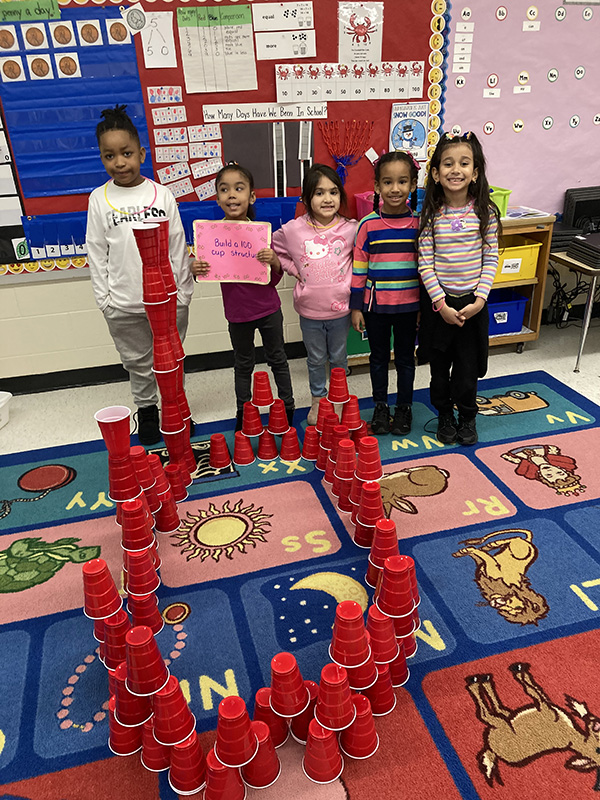 Five kindergarten kids stand and smile behind the structure they made out of red plastic cups.