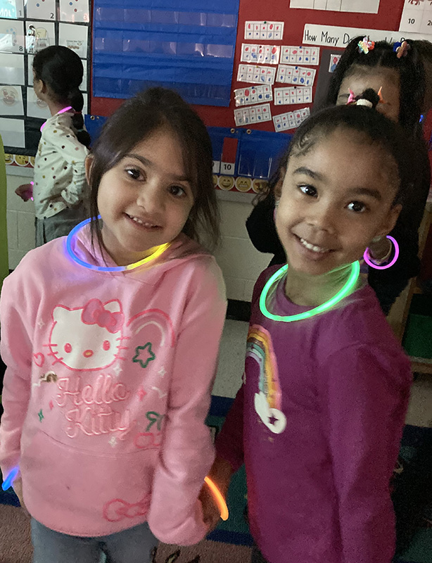 Two kindergarten girls with glow-in-the-dark necklaces smile.