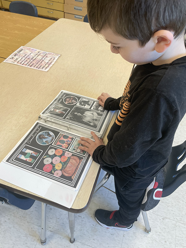 An elementary boy with short dark hair and a dark shirt looks through a book of artwork.