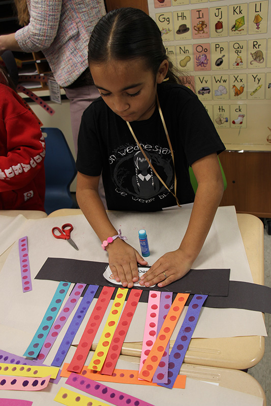 A girl makes a hat of paper - with 10 strips of paper with 10 dots on each.