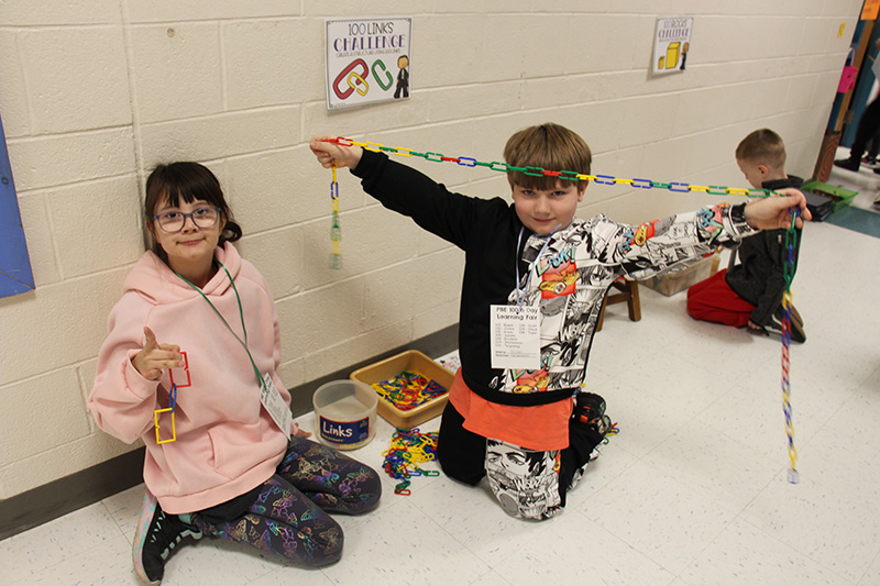 An elementary age boy holds up links of a chain he put together to make 100.