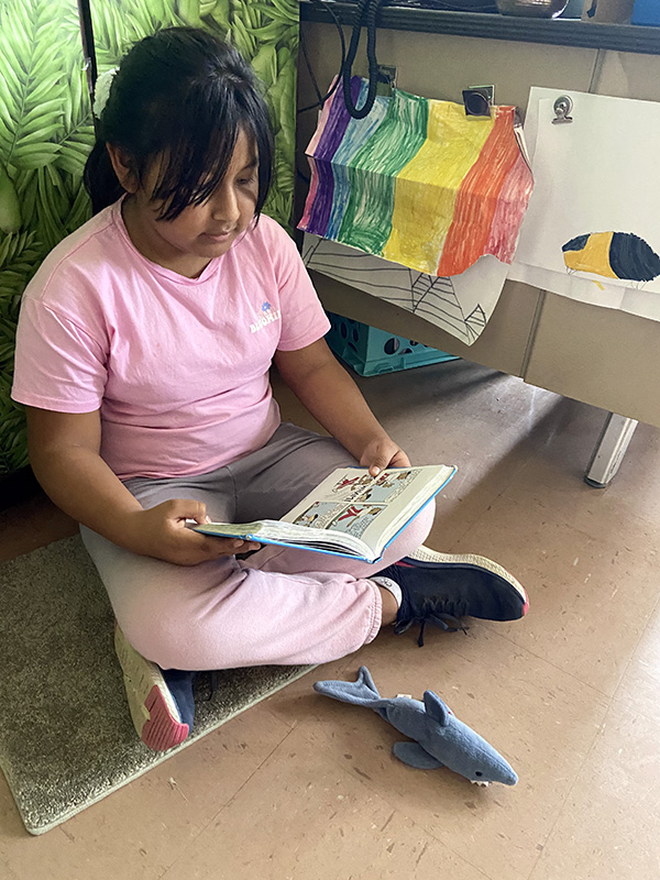 A girl sits cross-legged on the floor  reading a book.