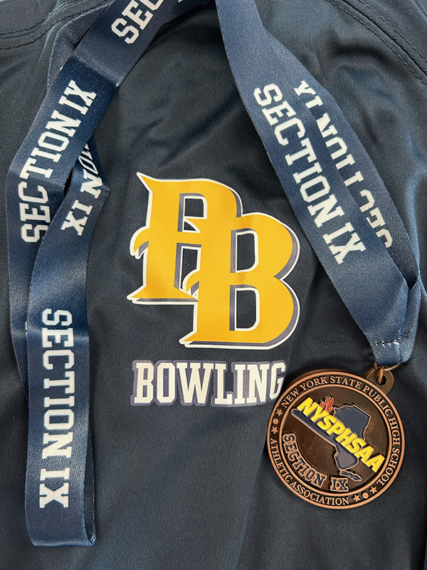 Blue fabric with a gold PB in the center with Bowling underneath it. There is a medal draped around it hat says Section IX