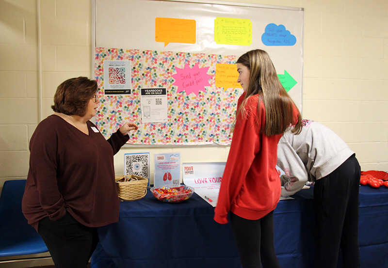 A young woman with long brown hair talks to a woman on the left who is explaining the dangers of vaping.