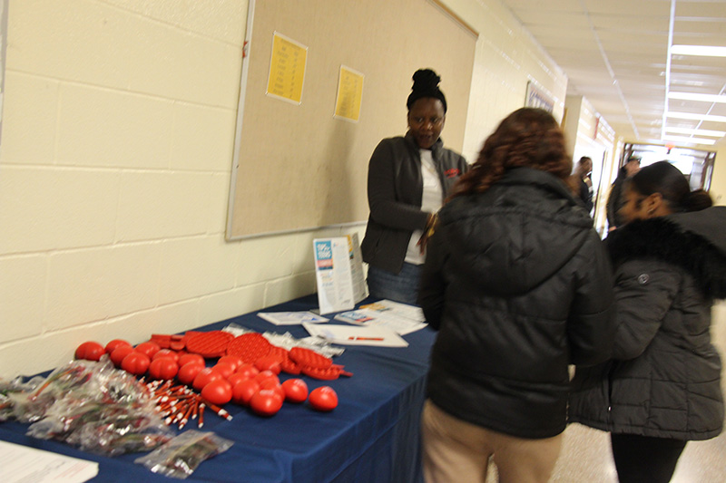 A woman stands by a table and talks to high school students about vaping.