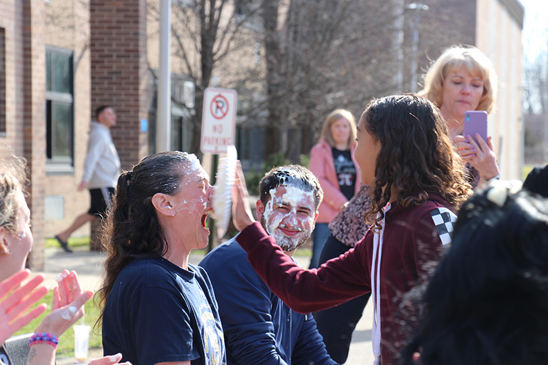 Just before it hits his face, a woman opens her mouth surprised as a pie comes to her face.