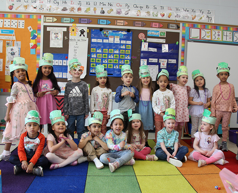 A cpre-K class all together, half sitting and half standing behind them. They all  have green headbands on they made for St. Patrick's Day.