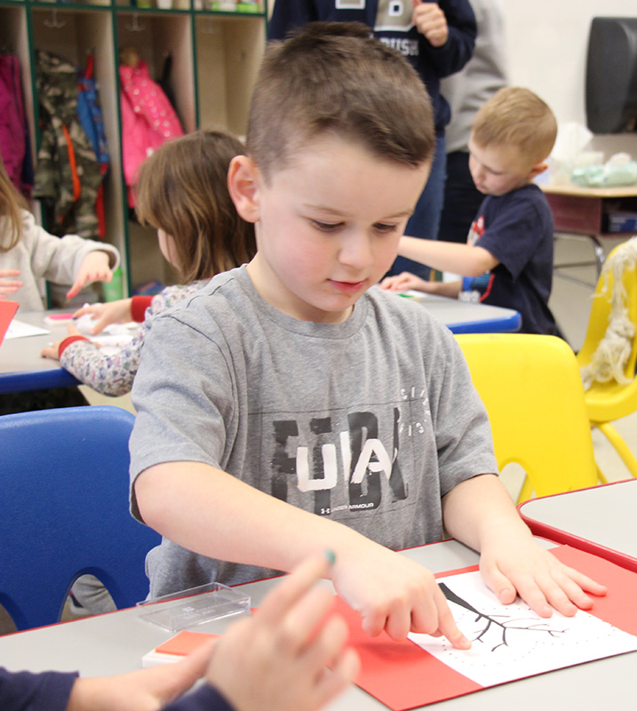 A boy with short brown hair uses his fingers to paint a tree on a piece of paper.