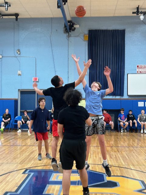 Middle school kids playing basketball go up for a jump ball.