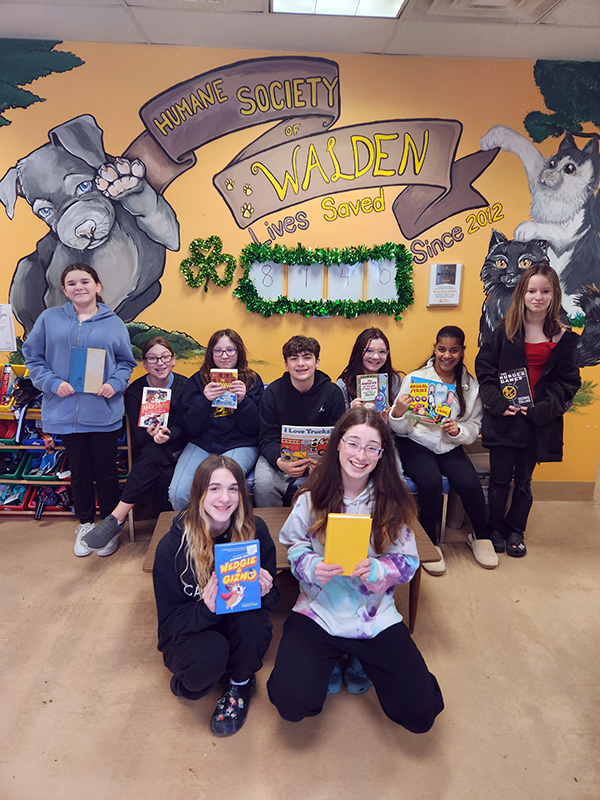 Nine middle school students stand and sit, holding up the books they've just read.