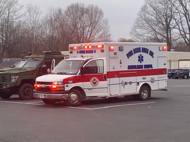 A white ambulance with lights on and blue writing on the side.