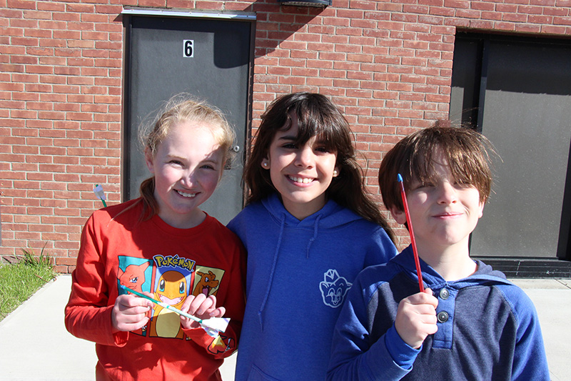 Three fourth-grade students stand holding little straw rockets they made.
