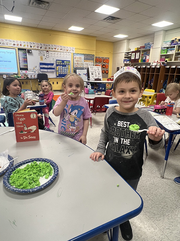 PreK students smile and eat green scrambled eggs.