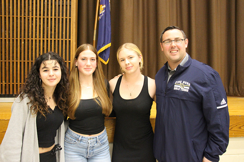 Three high school girls stand together smiling with a man on the right.