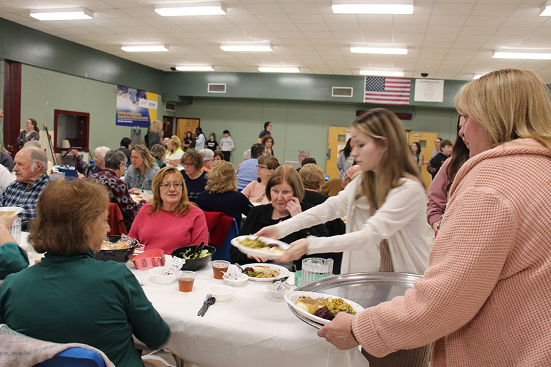 A young woman sets a plate down on a table in front of a group of senior citizens.