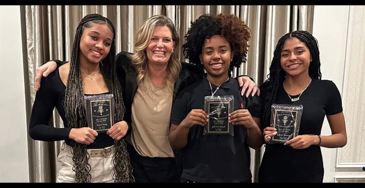 three high school girls smile and hold up plaques and a woman with her arms around two of them smiles too.