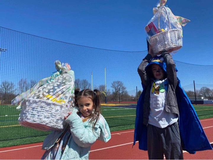 Two small kids hold large Easter baskets up over their heads.
