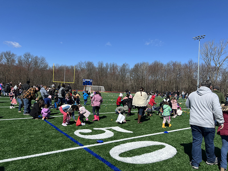 A large amount of kids and adults go onto a field to find Easter eggs.