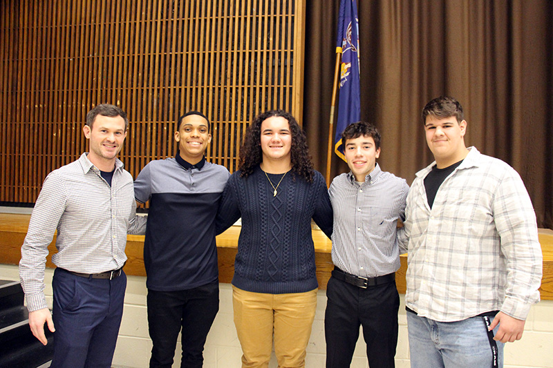 Four high school boys stand with a man on the left in front of a stage.