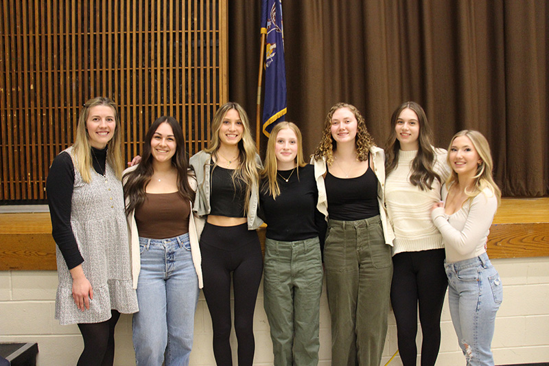 Six high school girls stand together smiling with a woman who is standing on the left.