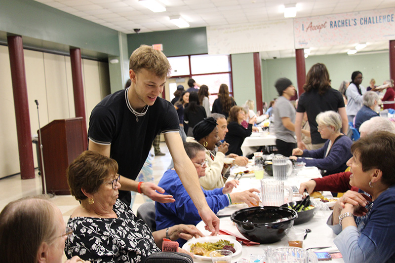 A young man puts a plate of food in front of a woman.