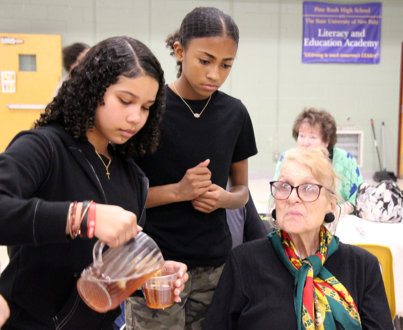 Two young women pour a glass of iced tea for a woman.