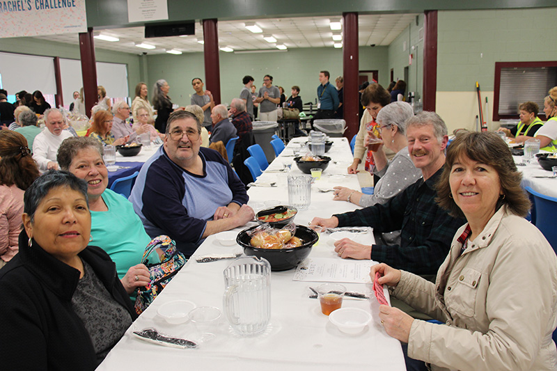 A long table with senior citizens sitting at it. They are smiling.