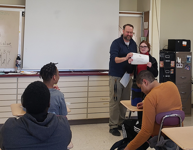 A young woman accepts a certificate from a man who has short dark hair and mustache.