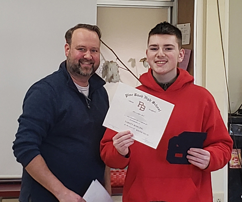A man with dark hair an mustache smiles next to a high school boy with short hair holding a certificate. The young man is wearing a red hoodie.
