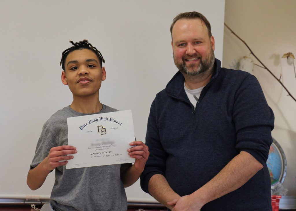 A young man smiles and holds up his certificate. He is standing next to a man who is also smiling.