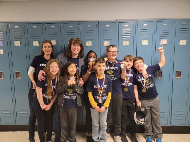 A group of seven elementary age kids and two women stand together smiling.
