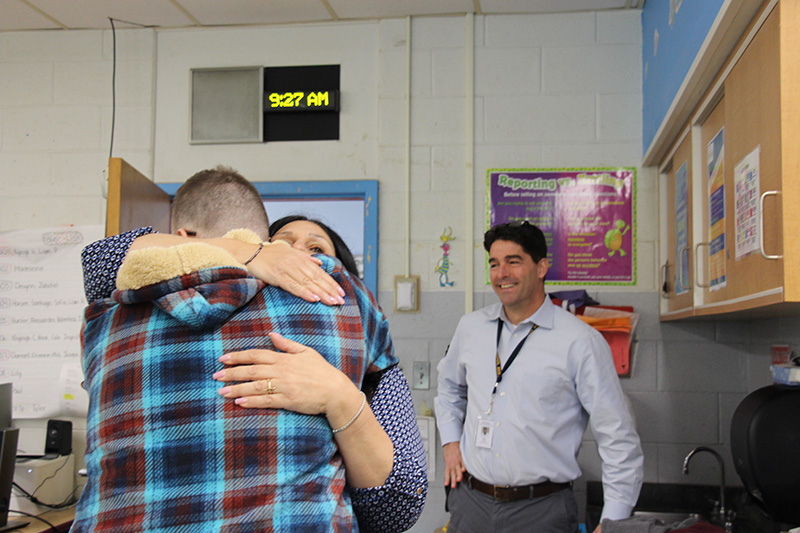 A woman and man hug as another man on the right looks on and smiles.