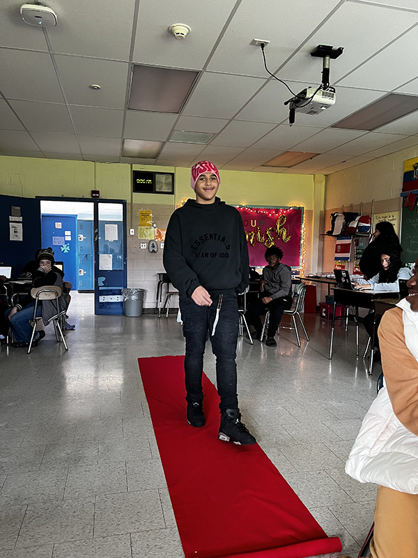 An eighth grade student walks a red carpet in a classroom.
