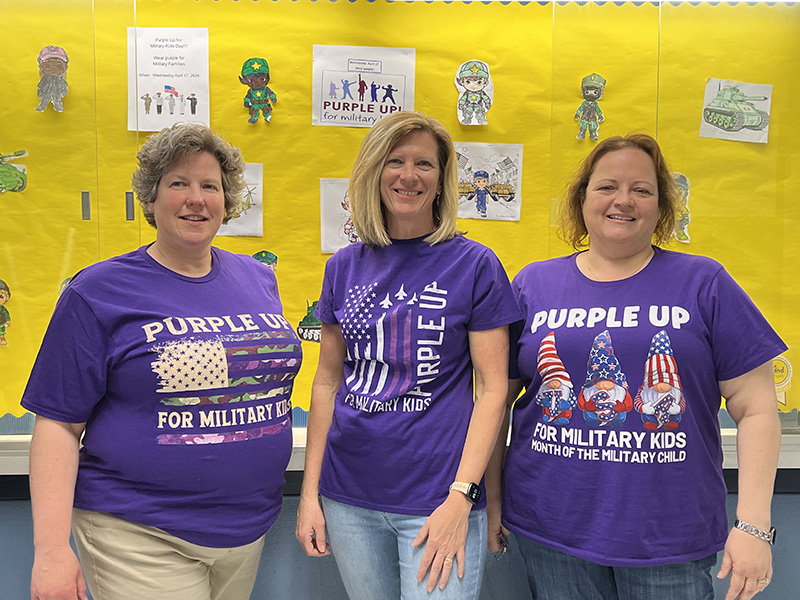Three women stand together wearing purple shirts that all say something about Purple Up day.