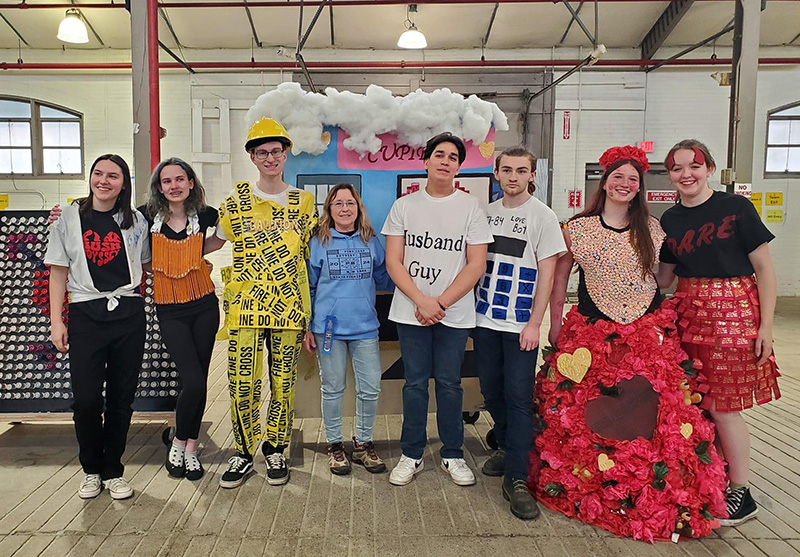 A group of seven high school students in very colorful and different costumes, stand together smiling.