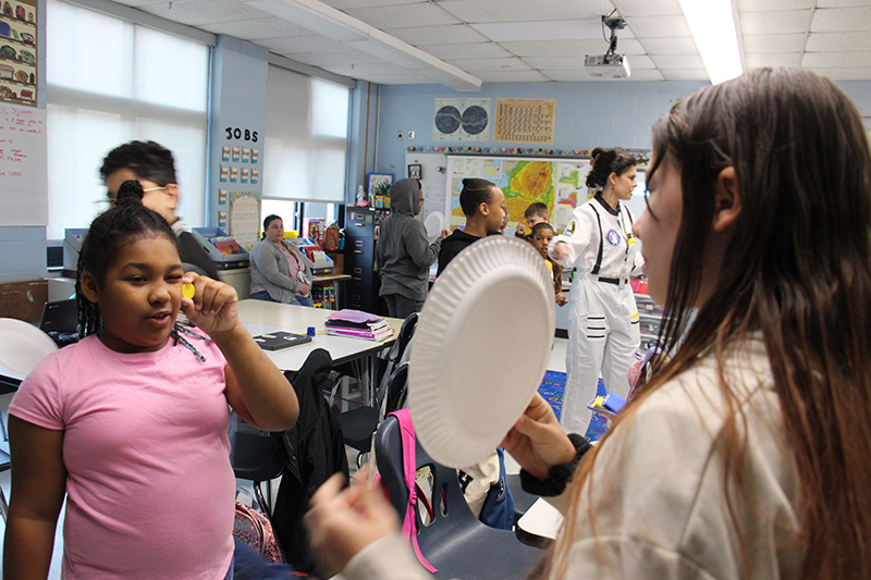 Older elementary students use a paper plate and a small cut out for the moon to show what will happen during the solar eclipse.