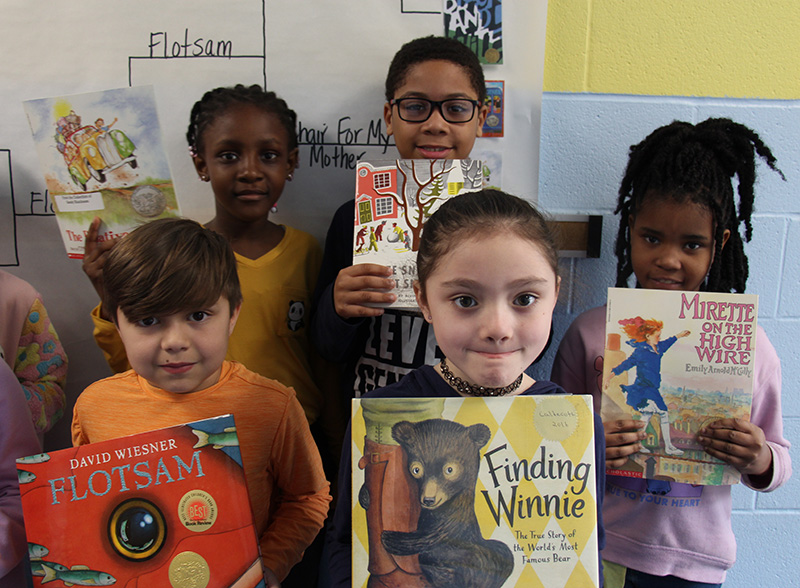 Five second-grade students stand together each holding a book.