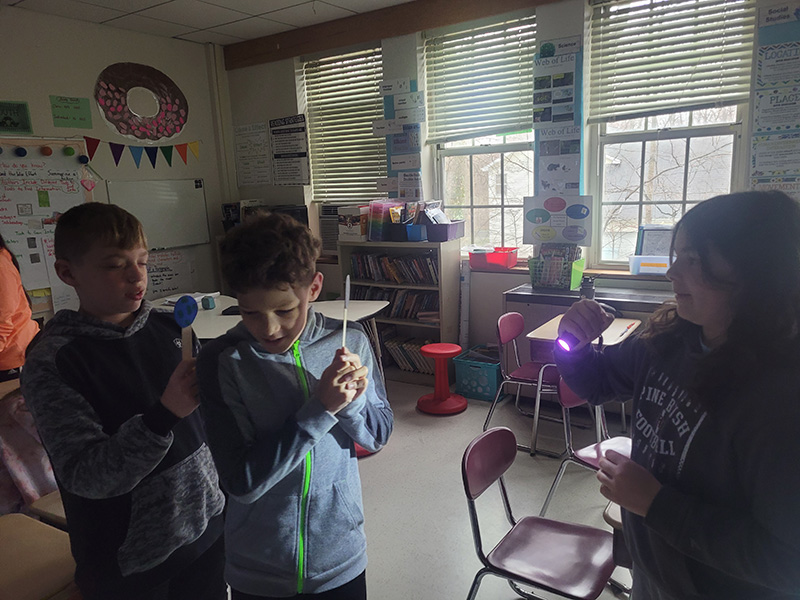 Students stand with flashlights and cut outs to show how an eclipse happens.