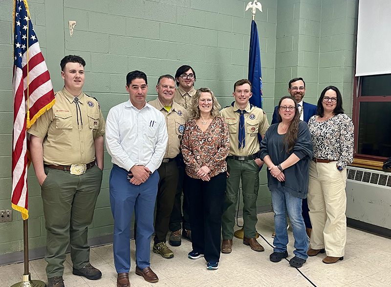 Three high school boys stand with six adults. The boys are wearing scout uniforms.