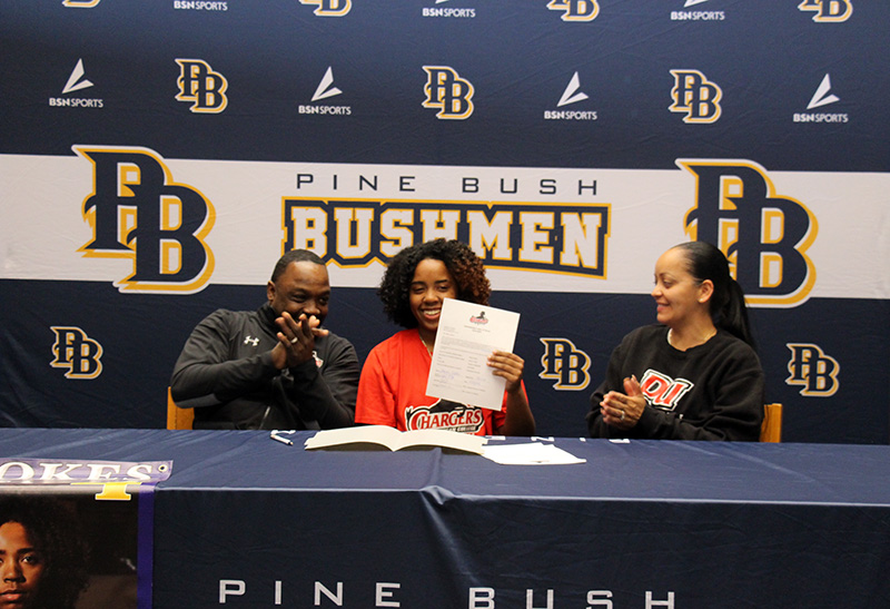 A young woman holds up a piece of paper, while her parents on either side of her clap and smile.