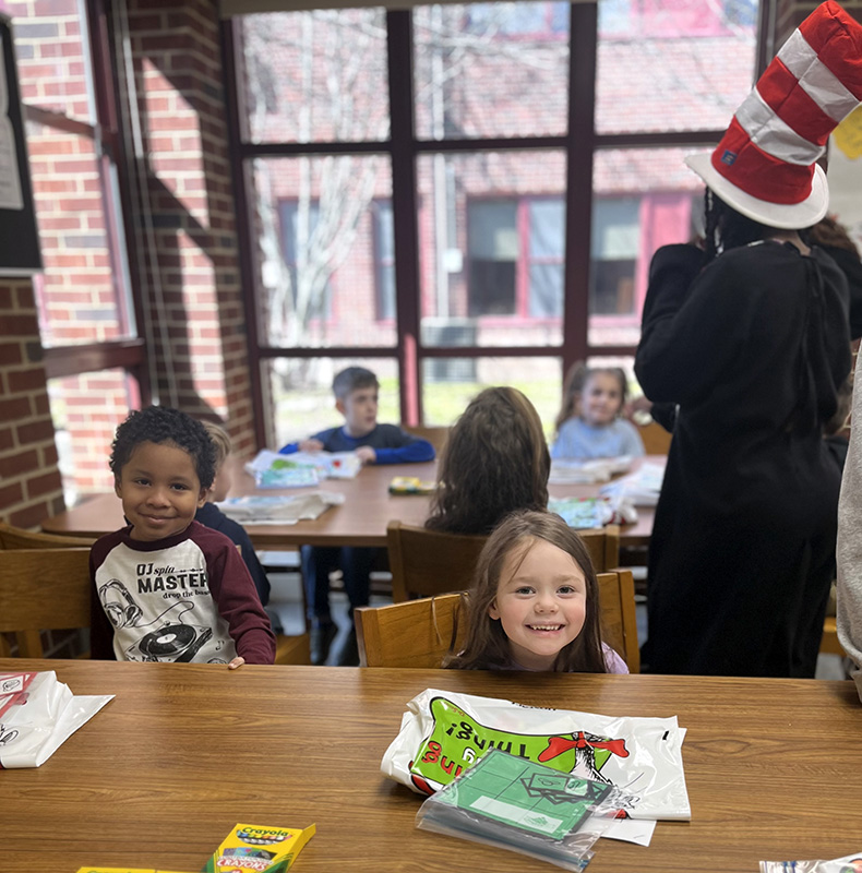 A boy and girl sitting at a table smile with their coloring.