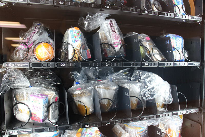 In a vending machine, there are clear plastic bags with different breakfasts - cereal, banana bread, yogurt.