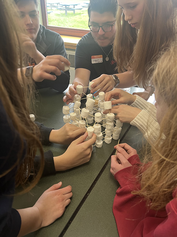 A group of high school kids build a structure from marshmallows and toothpics.